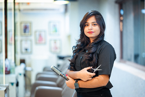 Portrait of young female hairdresser holding hair comb and scissor in salon