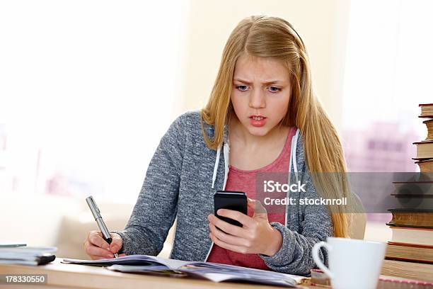 Preocupado Girl Reading Mensaje De Texto Mientras Que Haciendo Los Deberes Foto de stock y más banco de imágenes de Frustración