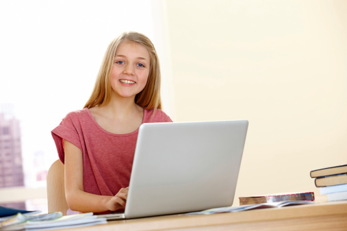 Smiling little school girl doing her homework on a laptop computer - Indoors