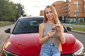 Relaxed young woman holds key standing in front of car