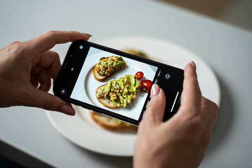 Close-up of a woman's hand photographing a fresh breakfast with a smartphone