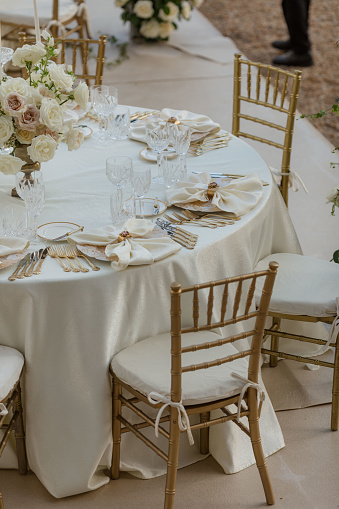 Stylish luxurious wedding table in white tones, with classic bouquets, silverware, white napkins.