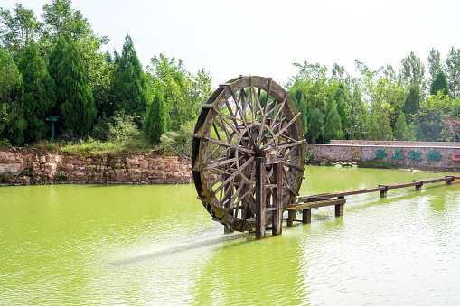 Wooden turbine baler or wood water wheels in creek canal for treatment water on pool pond at outdoor garden park at Wat Huay Pla Kang temple on sunset time in Chiang Rai, Thailand