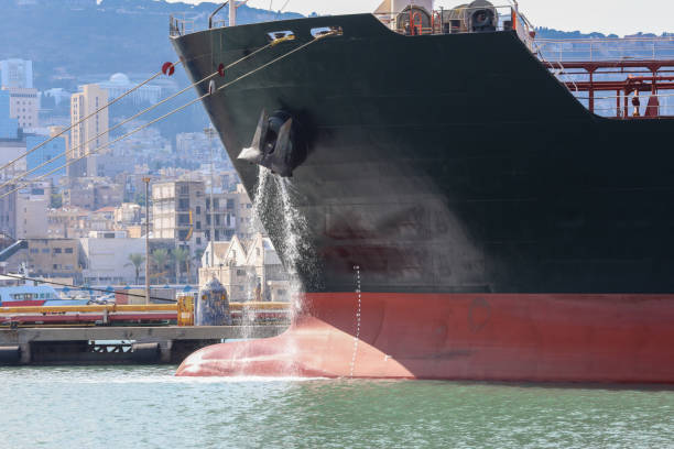 Large anchored cargo ship discharging ballast water out from Anchor's hub. Large anchored cargo ship discharging ballast water out from Anchor's hub. ballast water stock pictures, royalty-free photos & images