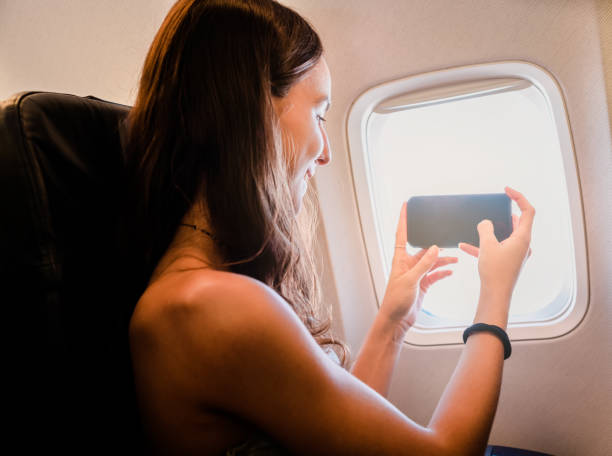 istock young girl using smartphone and looking through the window on airplane 1783330813