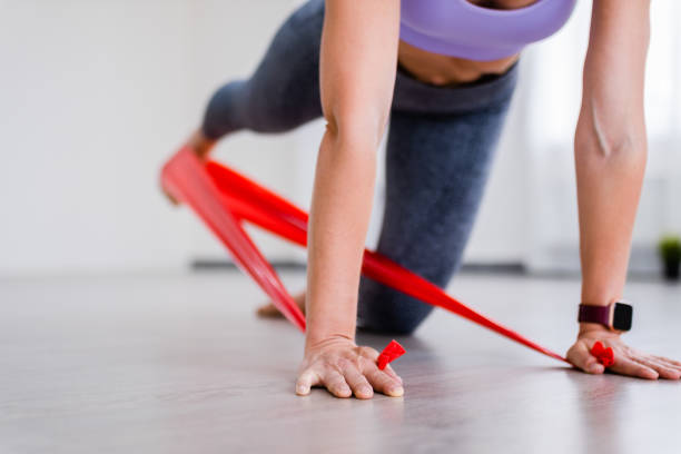 Athletic woman swings her leg back using red resistance band, kickback exercise of Pilates close up