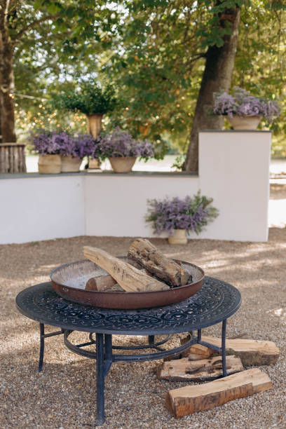 istock Open hearth with firewood installed on black wrought-iron table on gravel platform in park. 1783375271