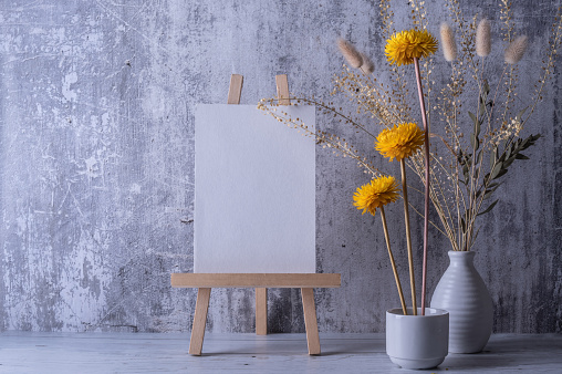 Template with blank white paper. Bouquet with dried yellow flowers in vase. Concrete background.