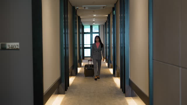 Asian businesswoman with suitcase walking through hotel corridor