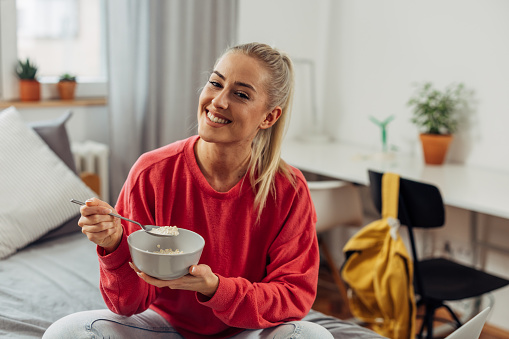 Happy young woman is eating oatmeal for breakfast