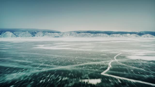 Fast flight over the ice of Lake Baikal, with a mountain range in the background. Olkhon Island, the Little Sea Strait. Baikal, Siberia, Russia. Drone aerial shot 4k