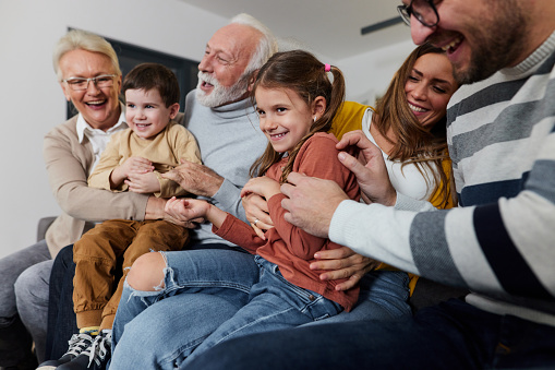 Cheerful extended family having fun while tickling in the living room.