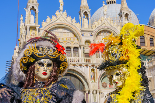 Venice, Italy - March 01, 2022: Couple dressed in traditional costumes stand in front of the Ducal palace, part of the Venice Mask Carnival, Veneto, Italy