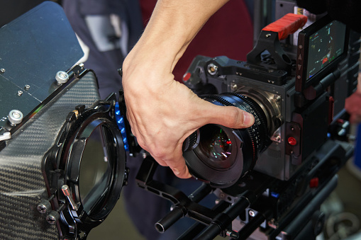 The hand of a videographer unscrews and removes the lens from a professional movie camera