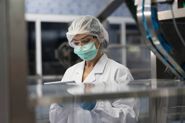 istock Female worker wearing uniform, hairnet and protective mask working inside automated conveyor belt production line in industry factory 1783443037