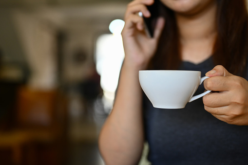 Cropped shot of young woman hand holding coffee cup and talking on mobile phone at cafe.