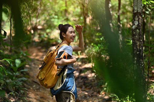 Smiling female traveller with backpack trekking in forest, exploring nature. Traveling, trekking and adventure concept.