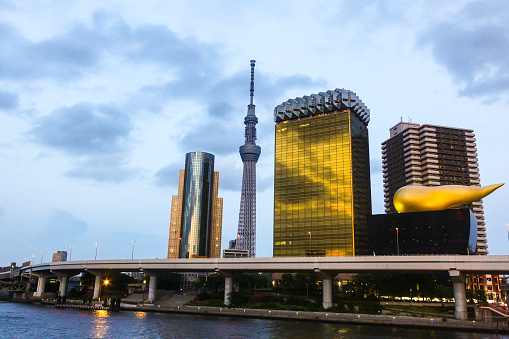 View of Asahi Group headquarter office building and Metropolitan Expressway and Sumida river and Azumabashi Pier at sunset from Azuma bridge with clouds in blue sky background.