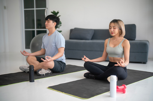 Young couple meditating in Lotus position in their new apartment.