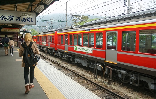 Hakone, Japan - May 2014: View of platform inside Hakone-Yumoto station with people walking and Tozan line red train and mountain in bright sky background.