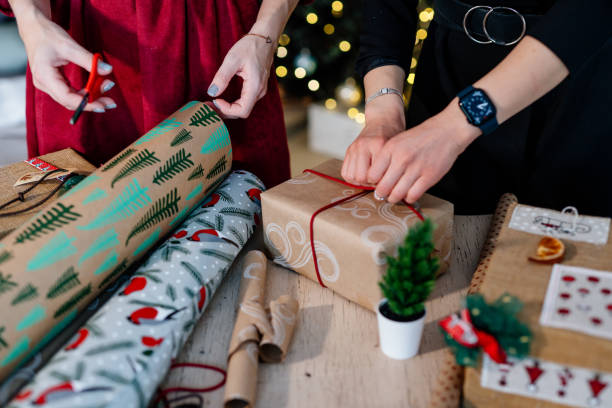 Two women hands wrapping Christmas gift boxes, close up.