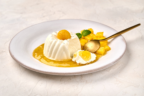 Spoon and piece of panna cotta with natural vanilla pod, mango syrup and mint, selective focus