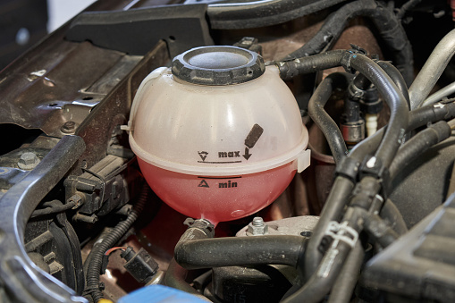 expansion tank of the car cooling system with pink antifreeze and black tubes of the engine compartment