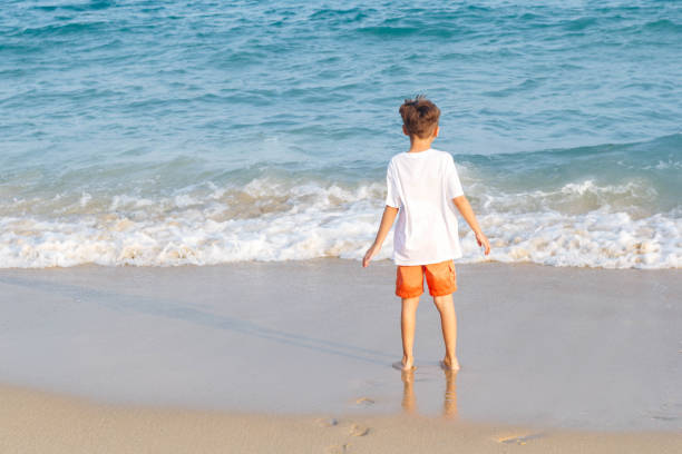 istock Boy in white tee-shirt standing alone on the seashore looking far away 1783529964