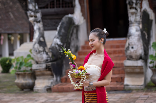 The act of lifting a tray of flowers over her head indicates that the woman is likely participating in a religious or cultural ceremony. Flowers are often used in Thai religious practices as offerings to deities or as part of traditional rituals.