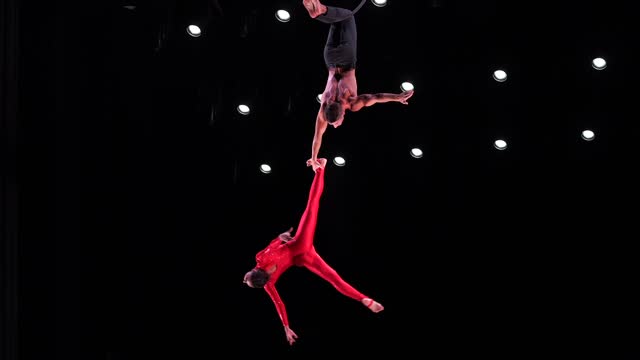 Circus aerial hoop duo with on black stage background performing trick, highly risky drop in slow motion. Concept of trust and confidence