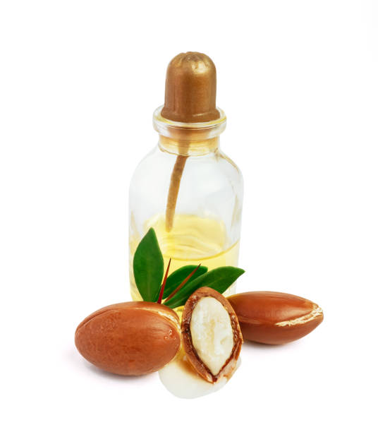 istock Three argan nuts with green leaves glass bottles on isolated white background. Chopped argan nut with a drop of oil. Whole and half Moroccan Argania Spinosa seeds for the production of oil 1783534816