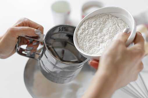 closeup of female hands sifting flour through sieve