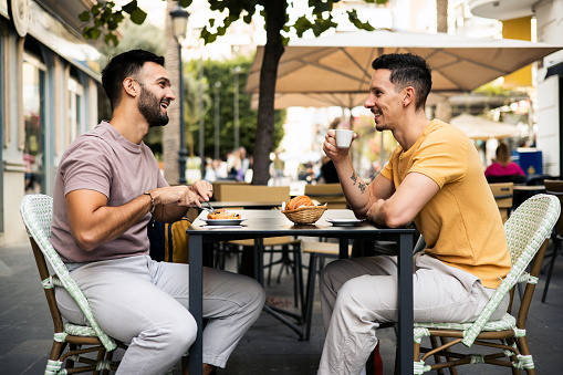 Happy gay couple having coffee and breakfast at the sidewalk cafe and enjoying their vacation in Valencia.