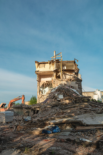 Demolition of ruined building. Excavator breaks old house damaged by terrorist attack, war or earthquake to build new house. Vertical orientation