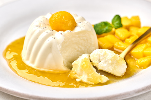 Macro spoon with piece of panna cotta with natural vanilla pod, mango syrup and mint, selective focus