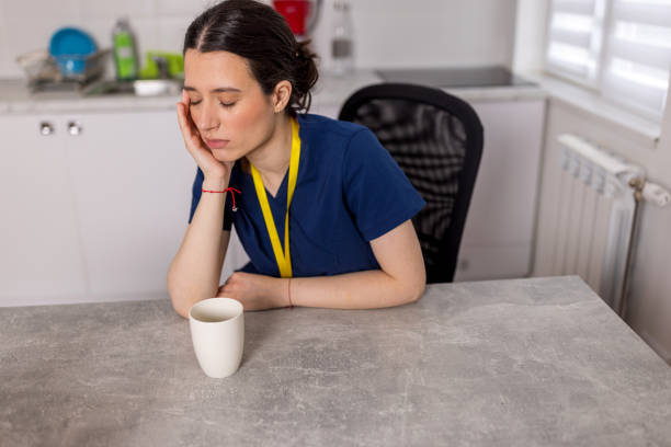 istock Young female nurse resting her head on her hand, while sitting at the kitchen table with a tiered look on her face. 1783566450