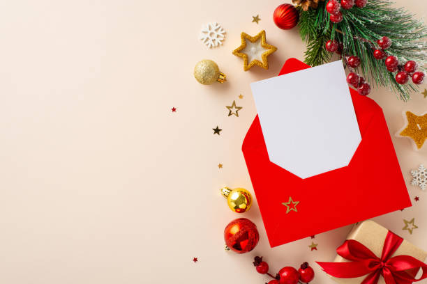 istock Get ready for holidays with wish list in red envelope surrounded by festive elements like gift box, gold ornaments, fir branch, holly berries, snowflakes on pastel beige backdrop with space for advert 1783567058