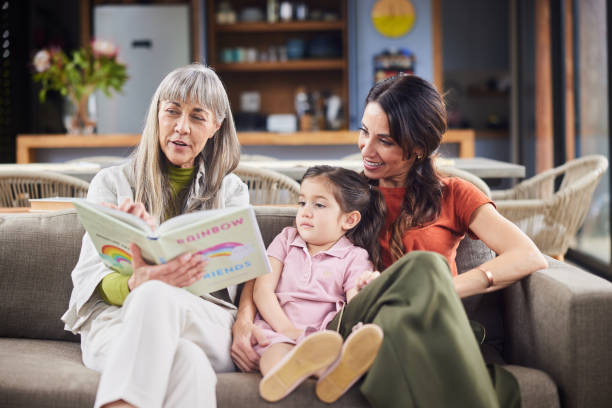 家でお母さんと一緒に座っている孫娘に読み聞かせをする年配の女性 - grandparent senior adult child reading ストックフォトと画像