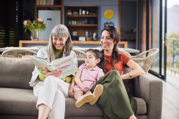 お母さんと一緒に座っている孫娘に本を読み聞かせる年配の女性 - grandparent senior adult child reading ストックフォ��トと画像