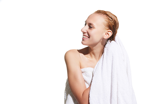 Girl standing in towel with wet hair after shower against white studio background. Drying hair with towel. Concept of beauty, hair care, treatment, natural cosmetics. Copy space for ad