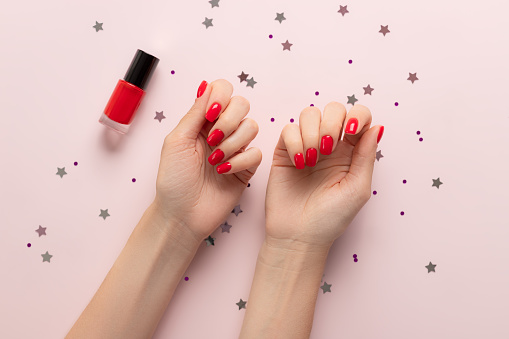 Beautiful female hand with red nail design on pastel background with confetti