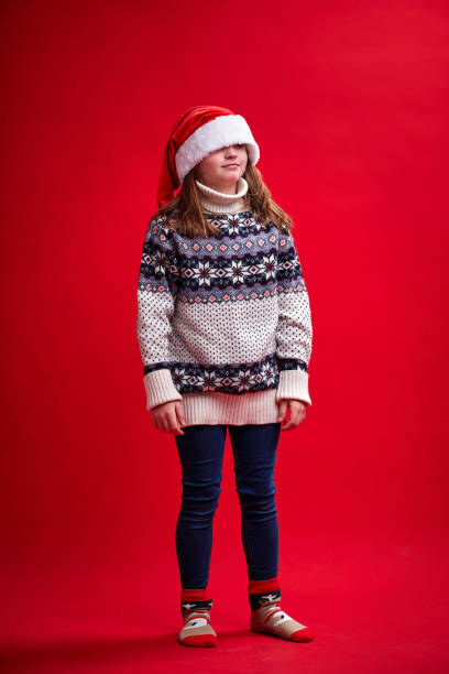 Cute little girl stands on red background with Santa's hat on her forehead stock photo