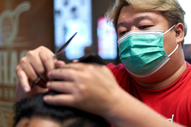 マスクをした理髪師が客の髪を切る顔に焦点をあてる - focus on face ストックフォトと画像