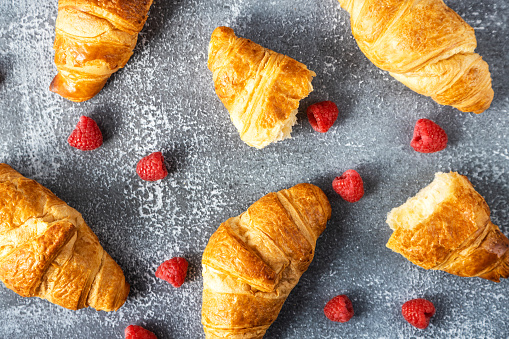 Fresh croissants with raspberries lie on a dark concrete background. View from above. Fresh pastries for breakfast