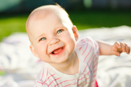 baby smiling and looking in camera outdoors in sunlight
