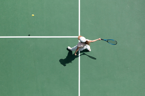 Overhead view of female tennis player playing match in tennis court.
