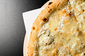 View on part of delicious creamy white pizza Quattro formaggi with gorgonzola, parmesan, mozzarella and ricotta cheese isolated on black