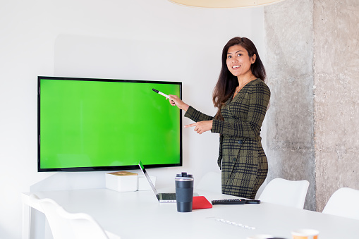 Content woman pointing at chromakey display in workspace