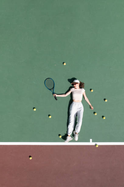 woman lying on a tennis court among balls with racket stock photo