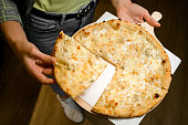 Restaraunt manager hold in hands wooden tray with fresh delicious pizza Quattro formaggi and separates one slice